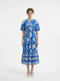 Woman wearing a blue floral print midi dress with puff sleeves and a tiered skirt, standing against a white background.