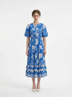 Woman wearing a blue floral print midi dress with puff sleeves and a tiered skirt, standing against a white background.