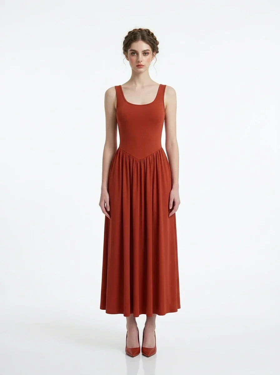 Woman wearing a rust-colored, sleeveless, ribbed knit maxi dress with a scoop neckline and gathered waist, standing against a white background.