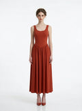Woman wearing a rust-colored, sleeveless, ribbed knit maxi dress with a scoop neckline and gathered waist, standing against a white background.