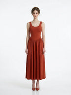 Woman wearing a rust-colored, sleeveless, ribbed knit maxi dress with a scoop neckline and gathered waist, standing against a white background.