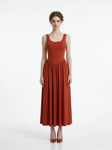 Woman wearing a rust-colored, sleeveless, ribbed knit maxi dress with a scoop neckline and gathered waist, standing against a white background.