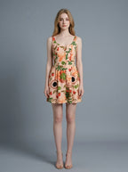Woman wearing a sleeveless, scoop neck, fit and flare A-line dress with an all-over print of strawberries, kiwis, flowers, and coffee cups, in a peachy-pink hue.