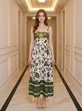 Woman wearing a white midi dress with a bird and floral print and green embroidered bodice, standing in a hallway.