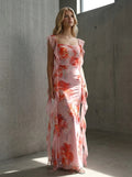 Woman posing in a pink floral print chiffon maxi dress with ruffle trim against a concrete wall