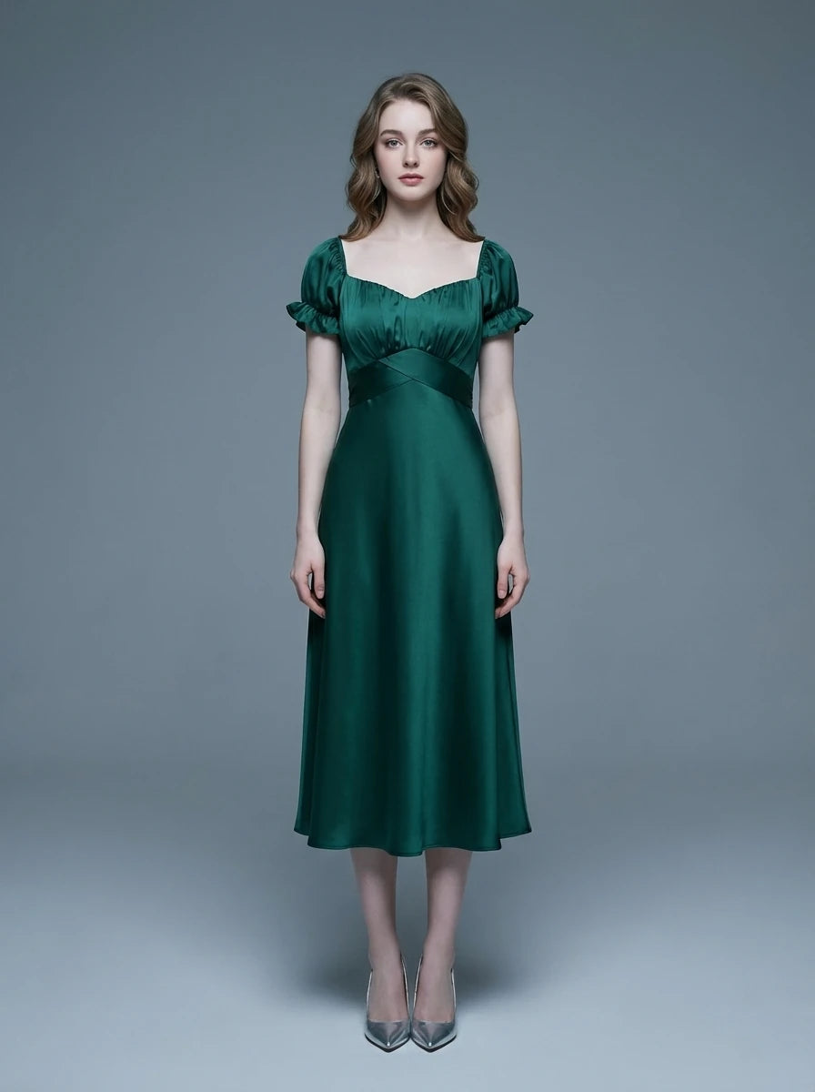 Woman wearing a green satin midi dress with puff sleeves and a square neckline, standing against a gray background.