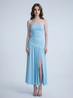 Woman wearing a sky blue strapless ruched jersey knit A-line evening dress with an asymmetrical hemline and side slit