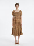 Woman wearing a tan midi dress with a smocked bodice and puff sleeves, featuring a sun and Greek key print.