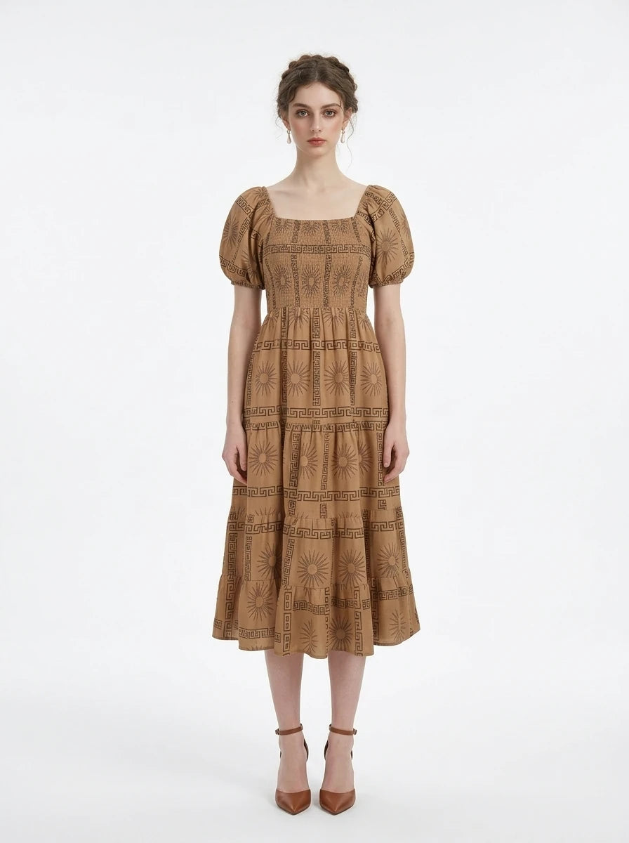 Woman wearing a tan midi dress with a smocked bodice and puff sleeves, featuring a sun and Greek key print.