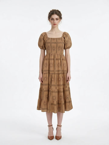 Woman wearing a tan midi dress with a smocked bodice and puff sleeves, featuring a sun and Greek key print.