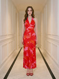 Woman wearing a long red halter neck dress with a tropical leaf print, standing in a hallway.