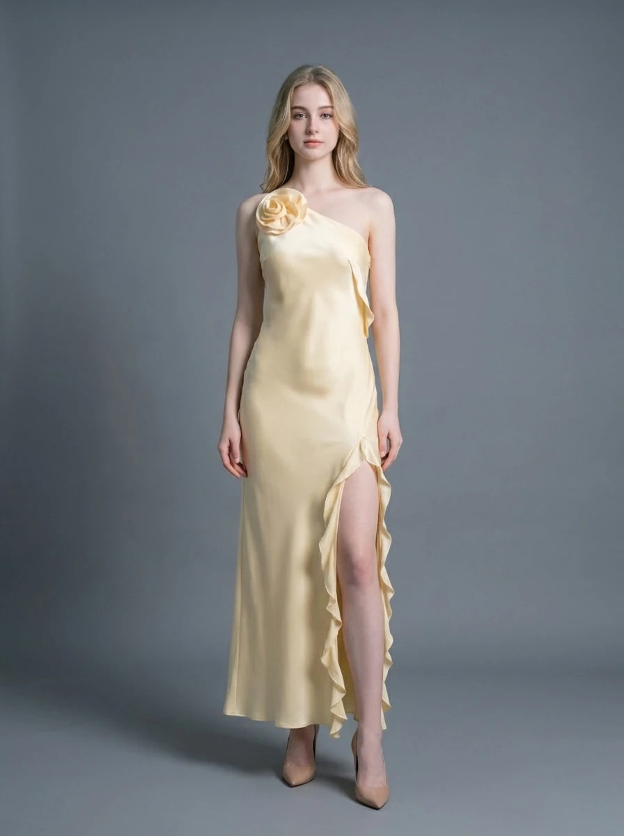 Woman wearing a pale yellow satin one-shoulder gown with a ruffled high slit and a floral applique on the shoulder.