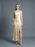 Woman wearing a pale yellow satin one-shoulder gown with a ruffled high slit and a floral applique on the shoulder.