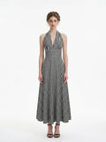Woman wearing a black and white gingham check halter neck maxi dress with a plunging V-neck and a defined empire waist, standing against a white background.