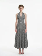 Woman wearing a black and white gingham check halter neck maxi dress with a plunging V-neck and a defined empire waist, standing against a white background.
