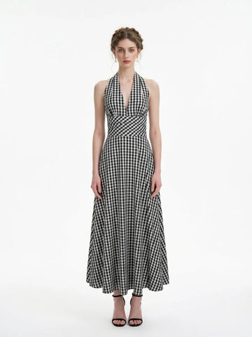 Woman wearing a black and white gingham check halter neck maxi dress with a plunging V-neck and a defined empire waist, standing against a white background.