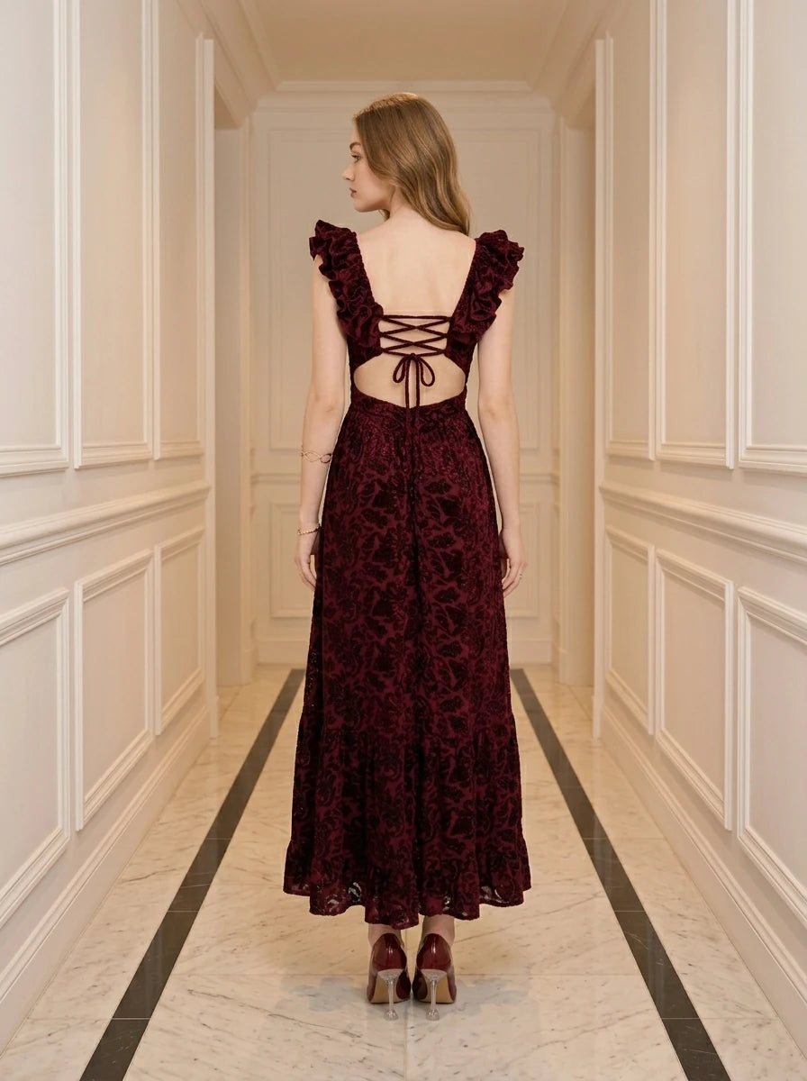 Woman wearing a burgundy velvet burnout A-line maxi dress with a V-neckline and ruffled cap sleeves, standing in a hallway.