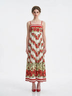 Woman wearing a white maxi dress with a red floral print and red trim, standing against a white background.