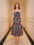 Woman wearing a navy floral print midi dress with spaghetti straps and a peplum waist, standing in a hallway.