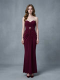 Woman in a burgundy strapless ruched maxi dress with gold waist embellishment, standing against a grey backdrop.