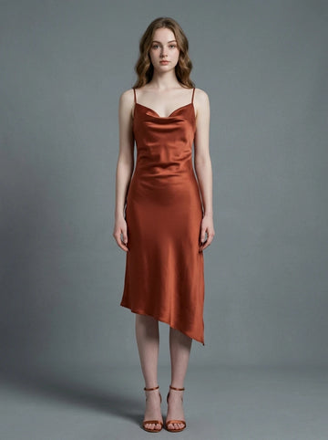 Woman wearing a rust-colored satin slip dress with spaghetti straps and a cowl neckline, standing against a grey background.