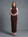 Woman wearing a long brown sleeveless mock neck dress with a knotted waist detail.