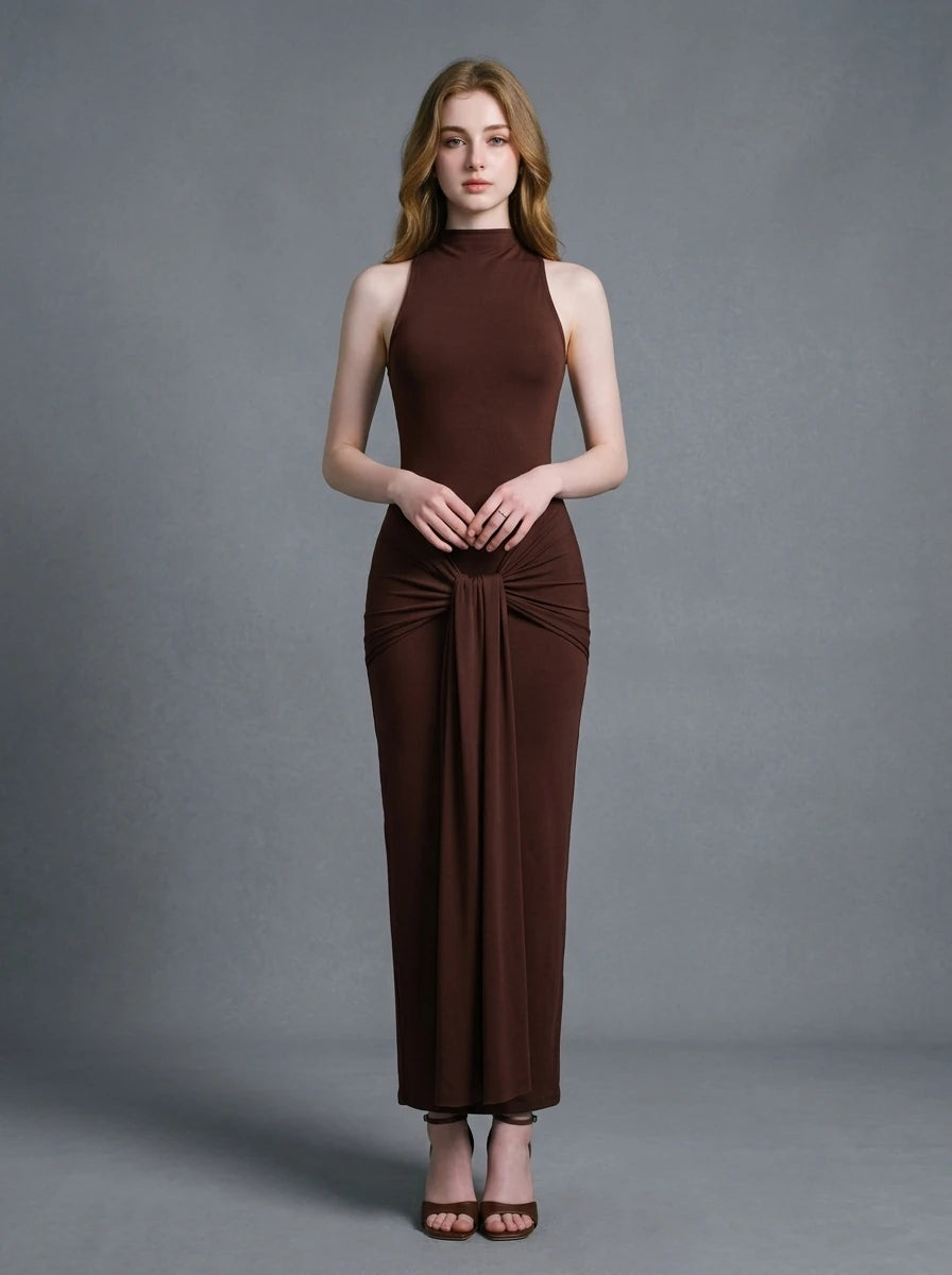 Woman wearing a long brown sleeveless mock neck dress with a knotted waist detail.