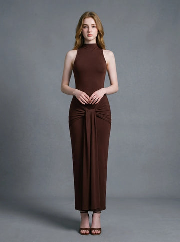 Woman wearing a long brown sleeveless mock neck dress with a knotted waist detail.