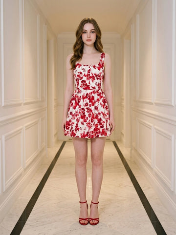Woman wearing a red and white floral print sleeveless fit and flare dress with a square neckline, standing in a hallway.