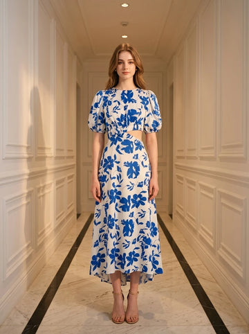 Woman wearing a white and blue floral print midi dress with puff sleeves and a cut-out waist, standing in a hallway.