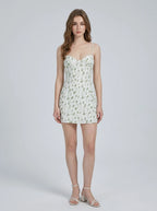 Woman wearing a white floral print mini dress with spaghetti straps and a sweetheart neckline.