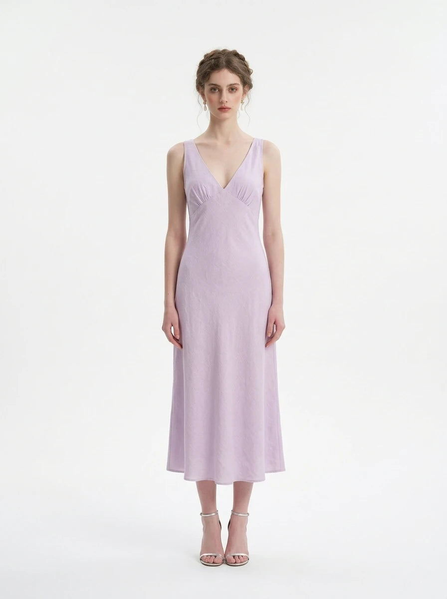 Woman wearing a lilac midi dress with a V-neckline and sleeveless design, standing against a white background.