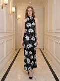 Woman wearing a black maxi dress with a white floral print and a halter neckline