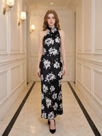 Woman wearing a black maxi dress with a white floral print and a halter neckline