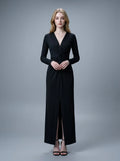 Woman in a black long-sleeved V-neck gown with a front knot and high slit, standing against a grey backdrop.