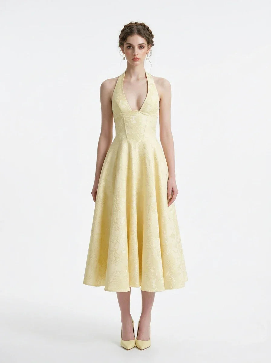 Woman wearing a pale yellow jacquard halter neck midi dress with a V-neckline and a corset back.