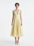 Woman wearing a pale yellow jacquard halter neck midi dress with a V-neckline and a corset back.