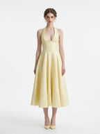 Woman wearing a pale yellow jacquard halter neck midi dress with a V-neckline and a corset back.