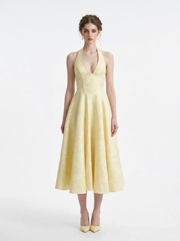 Woman wearing a pale yellow jacquard halter neck midi dress with a V-neckline and a corset back.