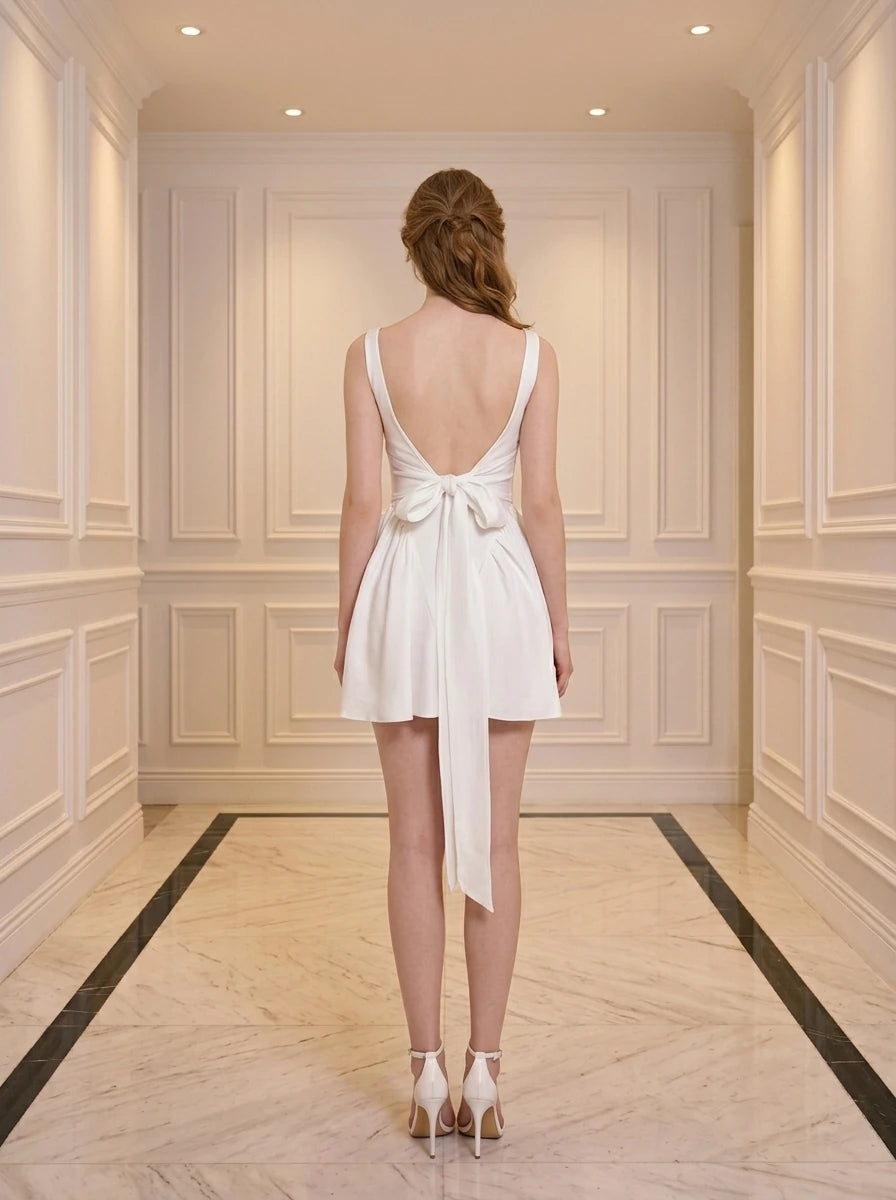 Back view of a woman in a white satin fit and flare dress with a square neckline and a large bow detail at the back.