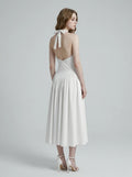 Back view of a woman in a white halter neck midi dress showcasing an open-back design.