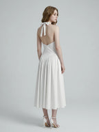 Back view of a woman in a white halter neck midi dress showcasing an open-back design.
