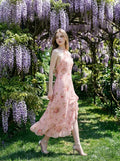 Woman in a pink floral print halter neck midi dress with ruffle trim and a high slit walking in a garden