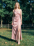Woman in a dusty rose satin one-shoulder maxi dress with a high slit, standing in a grassy outdoor area with trees in the background.