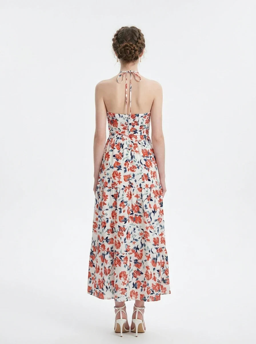 Woman wearing a white maxi dress with an orange and blue floral print, halter neckline, and tiered skirt.