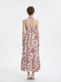 Back view of a woman in a white floral print maxi dress with a halter neckline.