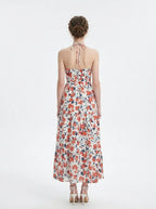 Back view of a woman in a white floral print maxi dress with a halter neckline.