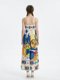 Back view of a woman in a white midi dress with a colorful abstract graphic print and gold chain spaghetti straps.