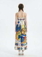 Back view of a woman in a white midi dress with a colorful abstract graphic print and gold chain spaghetti straps.