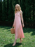 Woman walking on grass in a pink satin slip dress and straw bag.